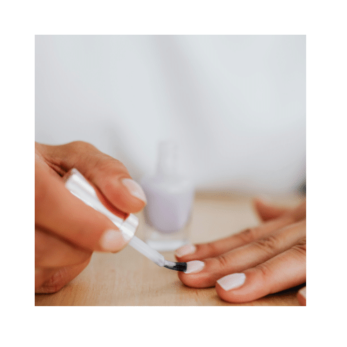 A close up of a person applying base coat on her nails. Prepping the nail before adding gel color for a lasting effect.