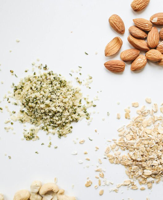 An assortment of almonds, cashews, hemp seeds, and oats neatly arranged on a white surface