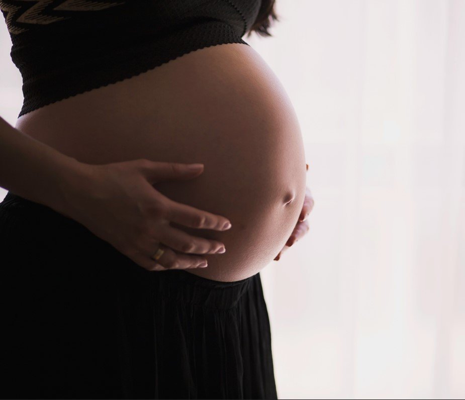 Close-up of a pregnant woman cradling her belly with her hands against a light background