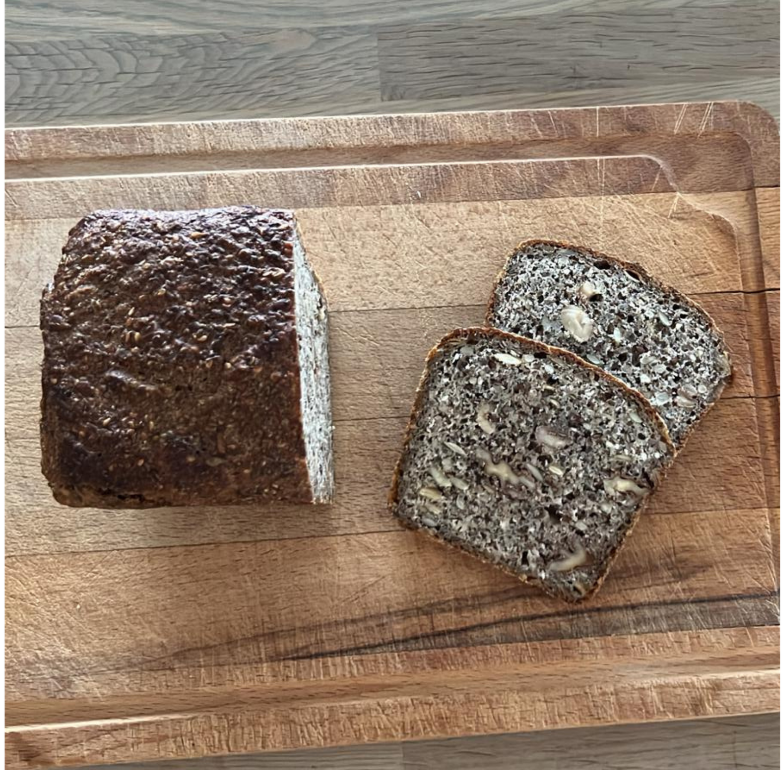 freshly baked sourdough seeded bread with two slices cut, displayed on a wooden cutting board.