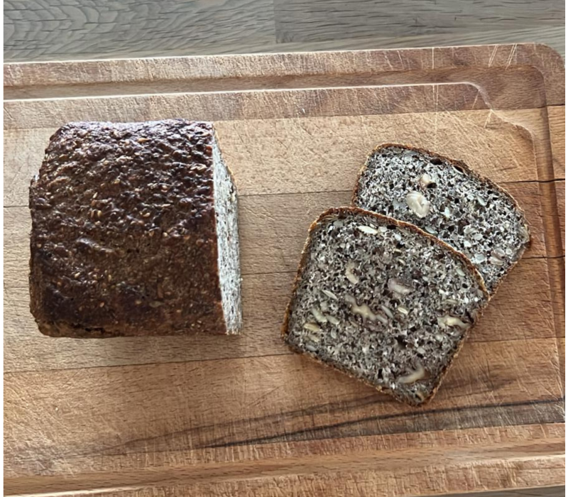 freshly baked sourdough seeded bread with two slices cut, displayed on a wooden cutting board.